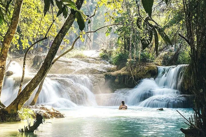 Eine Frau, die im leuchtend türkisen Wasser eines Kaskadenwasserfalls im Wald badet.