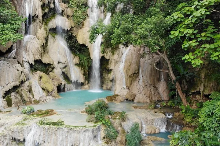 Impressive wide waterfall cascading down rocky cliffs into a turquoise pool surrounded by greenery.