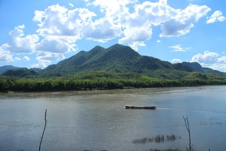 Ein Langboot, das auf einem breiten Fluss fährt, umgeben von üppig grünen Bergen.
