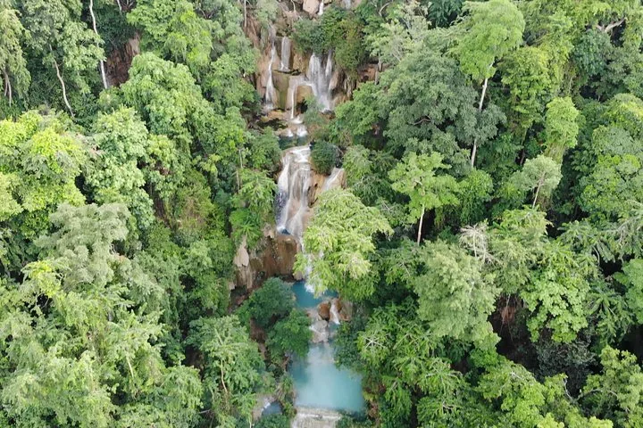 Aerial view of beautiful cascading waterfalls flowing down through dense green forest.
