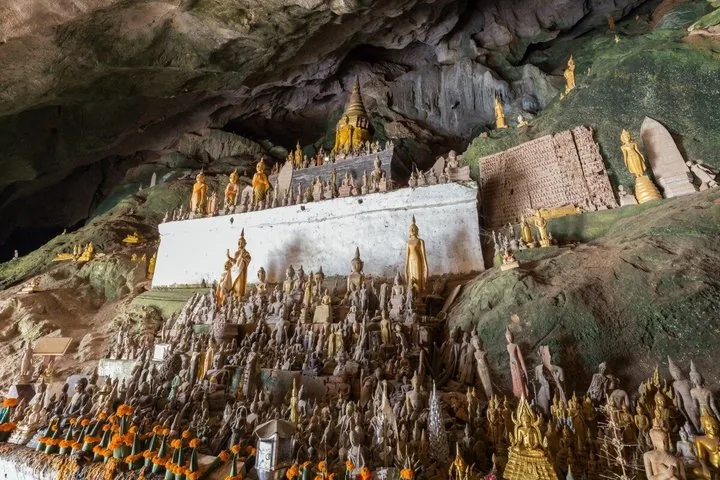 Hundreds of small Buddha statues clustered together inside a large rock cave, Pak Ou Caves.